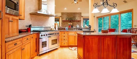 Une cuisine spacieuse avec des meubles en bois, un grand îlot central, des appareils électroménagers en acier inoxydable et un pare-feu en pierre.