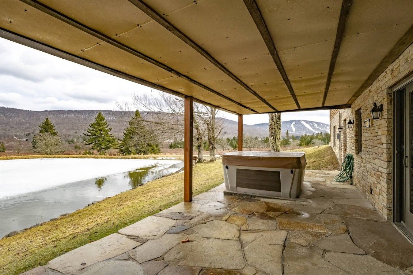 A stone patio with a hot tub, a stone wall, and a view of a lake and mountains.
