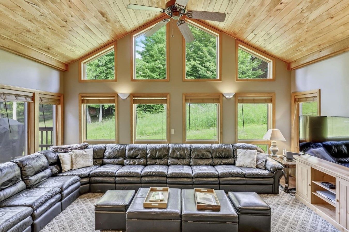 A spacious living room with a large leather sectional sofa, multiple windows, and a ceiling fan.