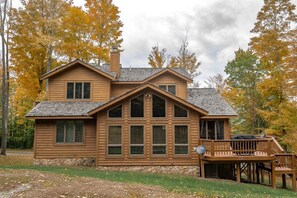 Une cabane en bois à deux étages, avec des fondations en pierre, de grandes fenêtres et une terrasse.