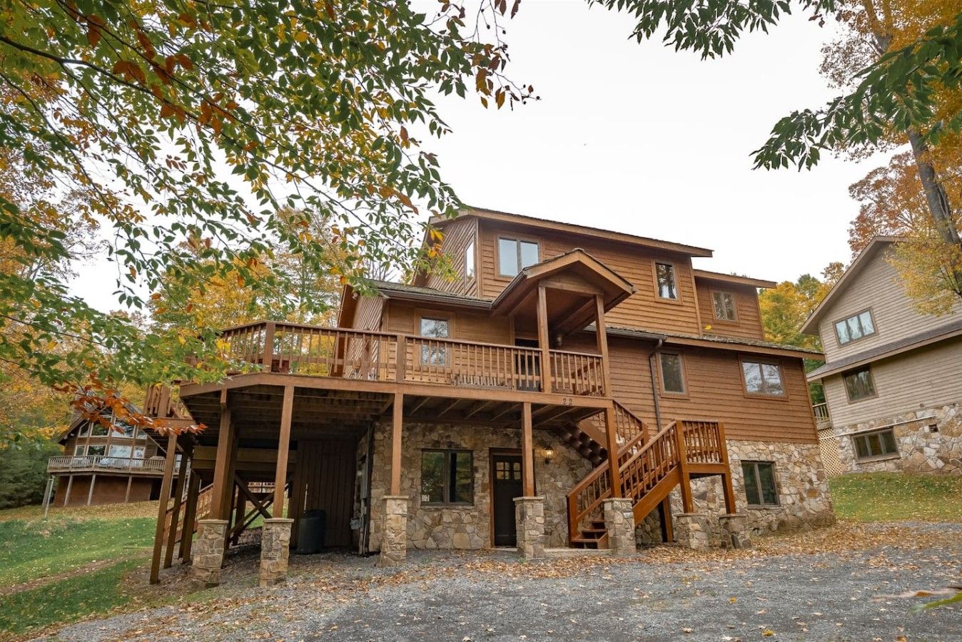 A two-story wooden cabin with a stone foundation, a covered porch, and a staircase leading to the upper level.