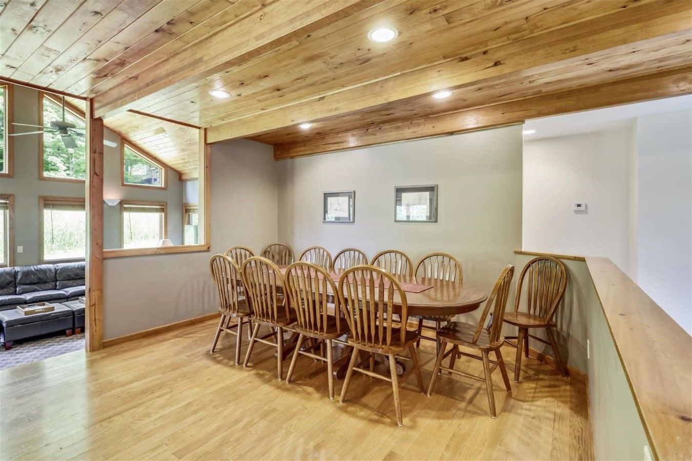A dining area with a wooden table and chairs, a sofa, and a window with a view of greenery.