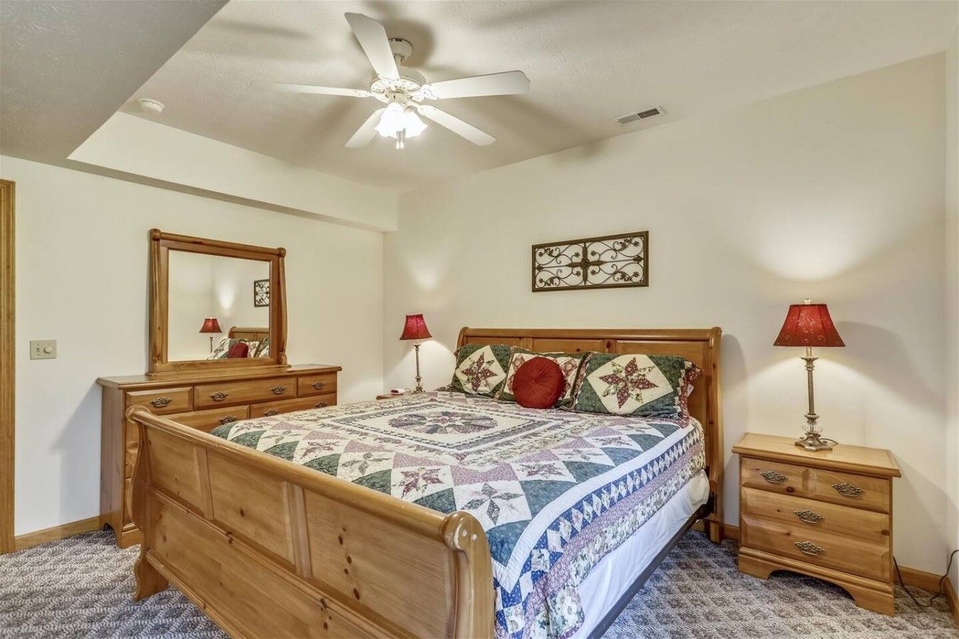 A bedroom with a wooden bed, two bedside tables, a ceiling fan, and a mirror.