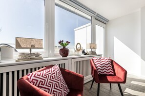 Una habitación luminosa con dos sillas rojas, un radiador y una ventana con vistas al cielo.