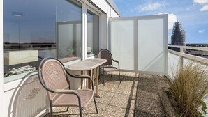 A balcony with a table and two chairs, a glass door, and a view of a cityscape. - Penthouse - Modern apartment with sea view, balcony, parking space, WLAN. Pets (Sylt)