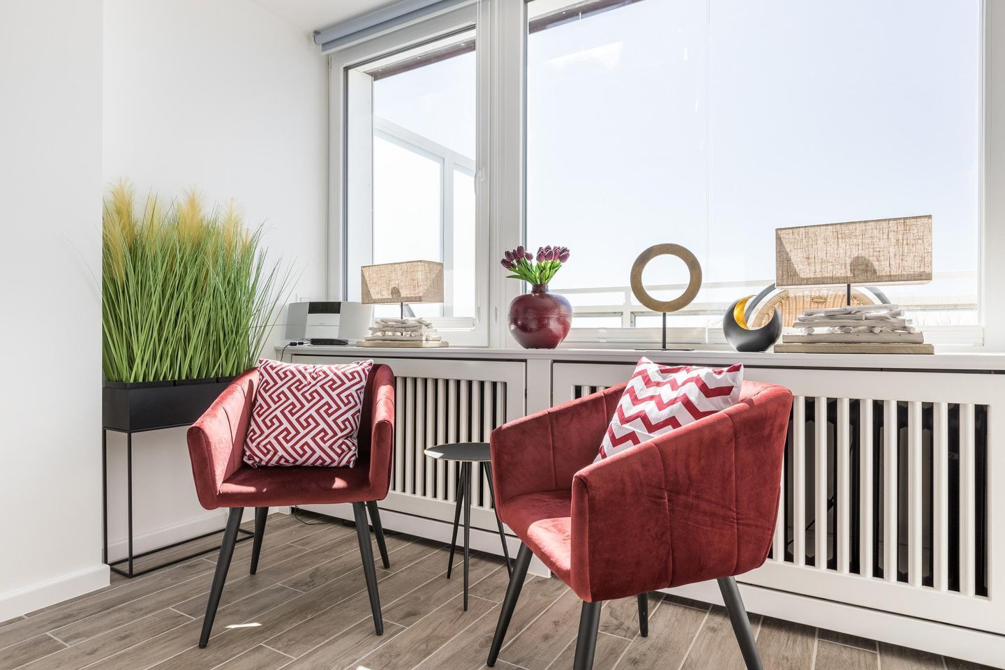 Ein modernes Wohnzimmer mit zwei roten Samt-Sesseln, einem kleinen runden Tisch und einer Topfpflanze.