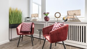 A modern living room with two red velvet armchairs, a small round table, and a potted plant. - Penthouse - Modern apartment with sea view, balcony, parking space, WLAN. Pets (Sylt)