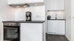 A modern kitchen with white cabinetry, a built-in oven, a coffee maker, and a kettle on the countertop. - Penthouse - Modern apartment with sea view, balcony, parking space, WLAN. Pets (Sylt)