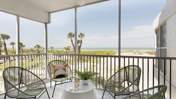 Un balcon donnant sur la plage, avec des chaises en métal et une petite table agrémentée d’une plante.
