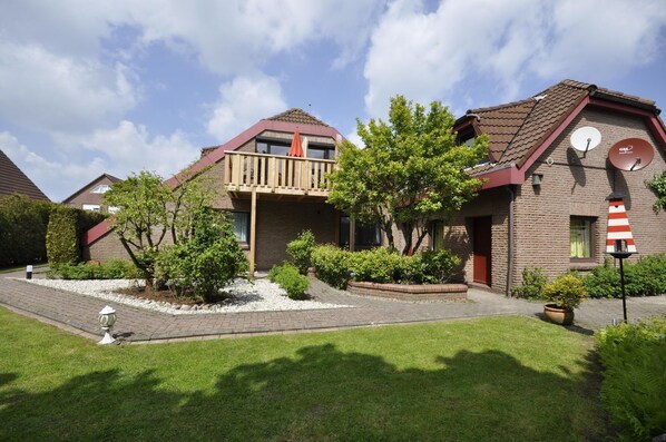 A two-story house with a balcony, a satellite dish, and a garden with various plants and a pathway.