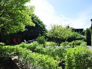 A garden area with various plants and shrubs, a pathway, and a building in the background.