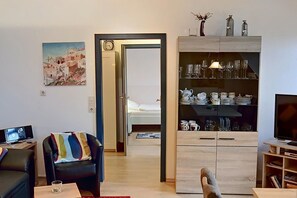 A living room with a TV, a bookshelf, a coffee table, a sofa, and a dining area with glassware and dishes.