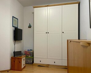 Et værelse med et hvidt skab, et træskab, et fjernsyn og et lille bord med en bærbar computer.