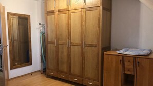 Ein Zimmer mit einem großen Schrank aus Holz, einem kleineren Korpus und einem Spiegel.