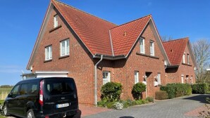 Ein zweistöckiges Backsteinhaus mit rotem Ziegeldach, ein schwarzes Auto auf der Auffahrt, und ein klarer, blauer Himmel.