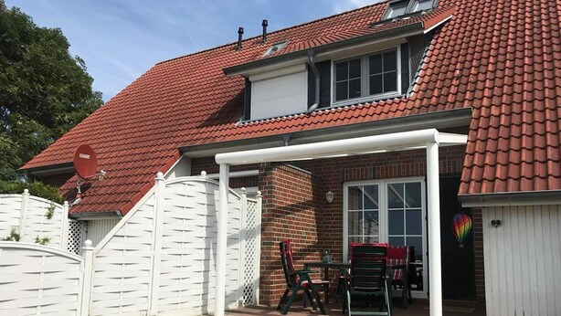 Ein Haus mit rotem Ziegeldach, einer Ziegelaußenfassade und einer überdachten Terrasse mit Gartenmöbeln.