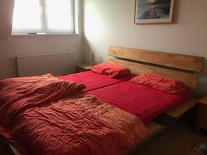 En seng med trægavl, to puder og et rødt tæppe.