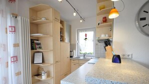 A kitchen with a granite countertop, wooden cabinets, a window with a view, and a clock on the wall.