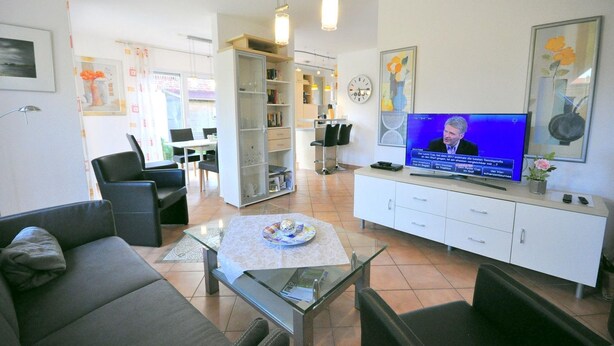 A modern living room with a television, seating, a glass coffee table, and a bookshelf.