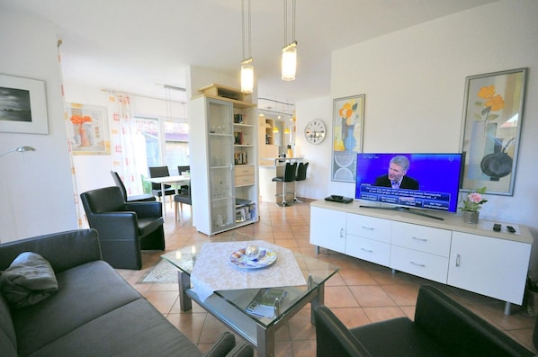 A modern living room with a television, seating, a glass coffee table, and a bookshelf.