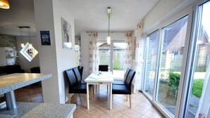 A dining area with a table and chairs, a kitchen area with a counter, and large windows with curtains.