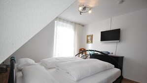 A bedroom with a bed, a TV, a window with curtains, and a ceiling light fixture.