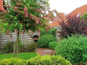 A garden with a wooden deck, a brick oven, and a variety of shrubs and trees. - Ferienwohnung Mühlenblick 5 EG Rechts (Wittmund)