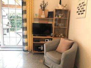 A living room with a television, a sofa, a bookshelf, and a window with curtains. - Ferienwohnung Mühlenblick 5 EG Rechts (Wittmund)