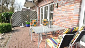 A patio area with a table and chairs, a brick wall, and a metal gate. - Vacation apartment Caspersweg 4a - Holiday apartment Fernblick Caspersweg 4a (Wittmund)