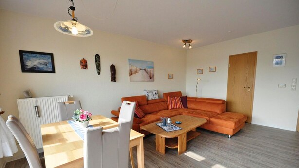 A living room with a sofa, a dining table with chairs, a radiator, and a door. - Vacation apartment Caspersweg 4a - Holiday apartment Fernblick Caspersweg 4a (Wittmund)