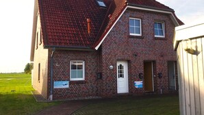 A two-story brick house with a red-tiled roof, a front door, and a small porch. - Vacation apartment Caspersweg 4a - Holiday apartment Fernblick Caspersweg 4a (Wittmund)