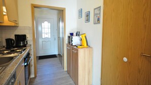 A kitchen with a stove, coffee maker, and microwave. There is a wooden cabinet and a door with a handle. - Vacation apartment Caspersweg 4a - Holiday apartment Fernblick Caspersweg 4a (Wittmund)