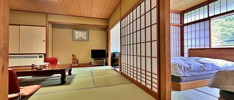 A traditional Japanese-style room with tatami flooring, a low wooden bed, a desk with a chair, a television, and a sliding shoji screen.