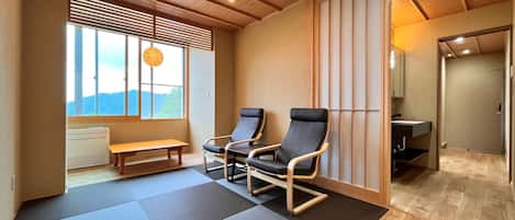 Una habitación con esteras de tatami, techo de madera, un banco, dos sillas, una ventana con persianas y vistas al exterior.