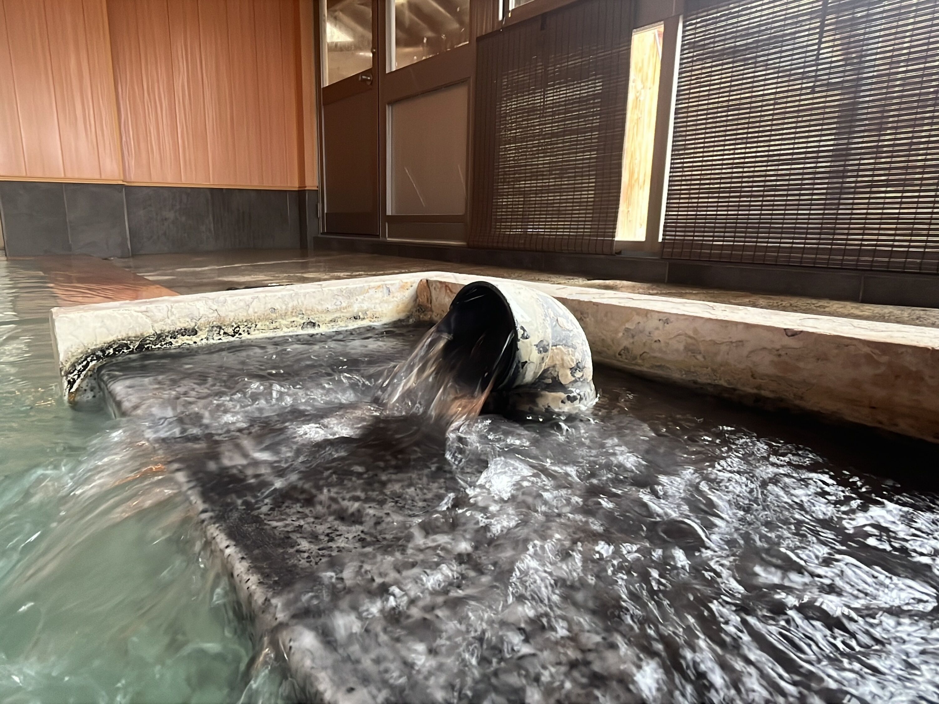 A hot spring area with a water channel, tiled flooring, and wooden paneling.