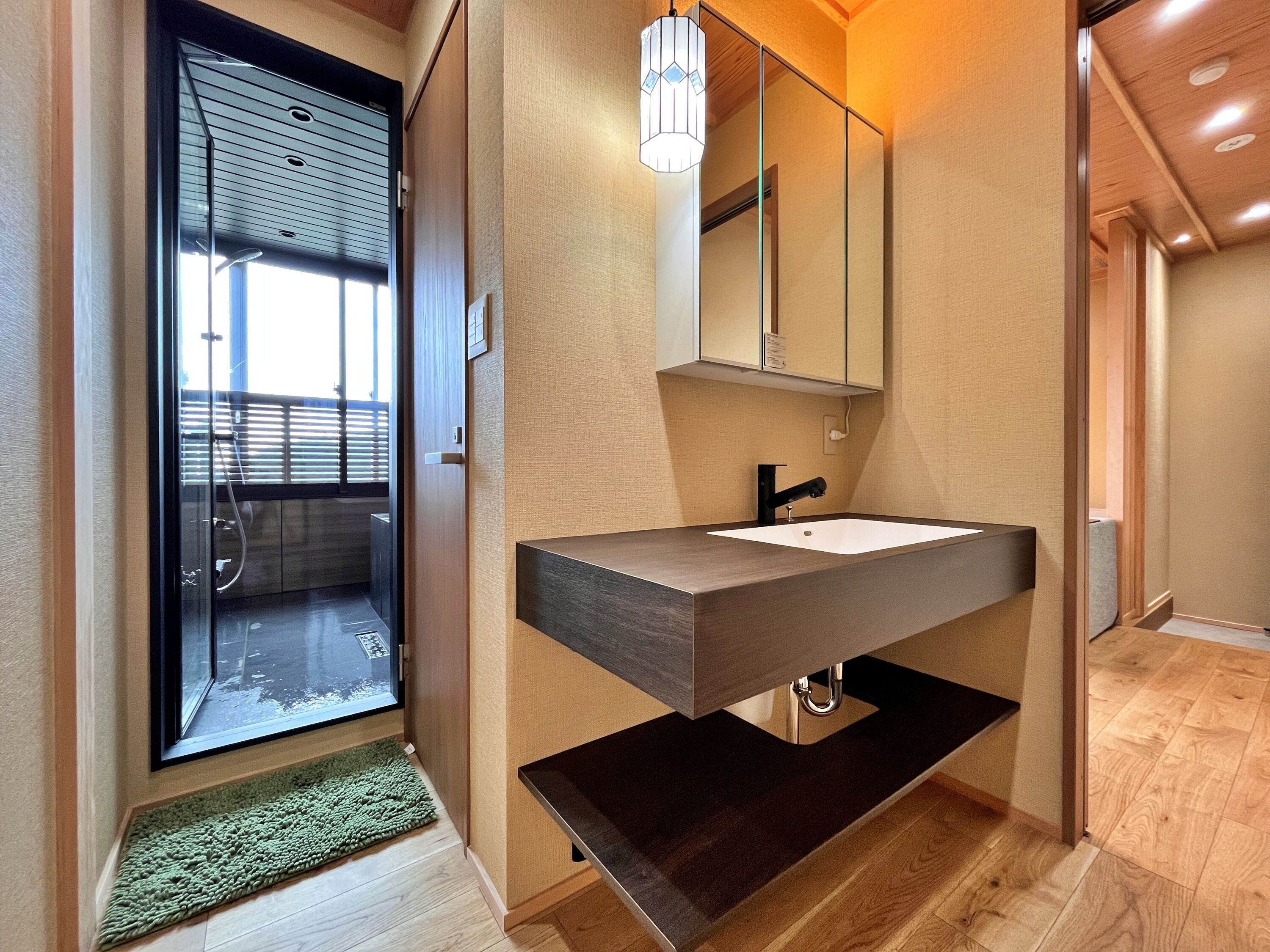 A modern bathroom with a wooden vanity, a large mirror, and a glass shower door.