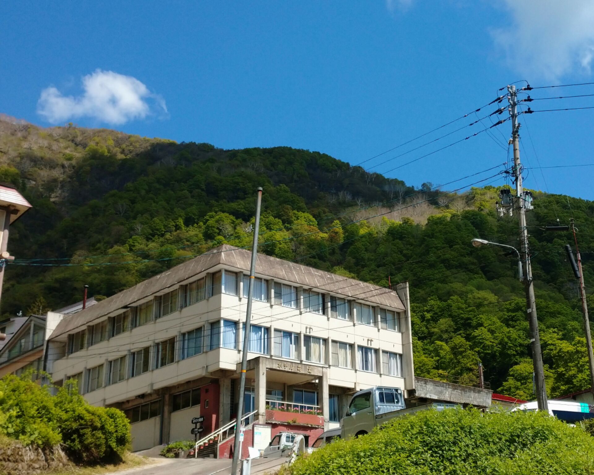 A multi-story building with a flat roof, surrounded by lush greenery and hills.