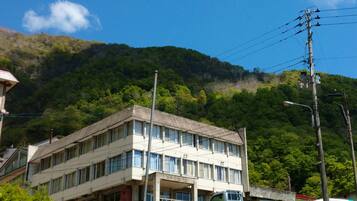 A multi-story building with a flat roof, surrounded by lush greenery and hills.