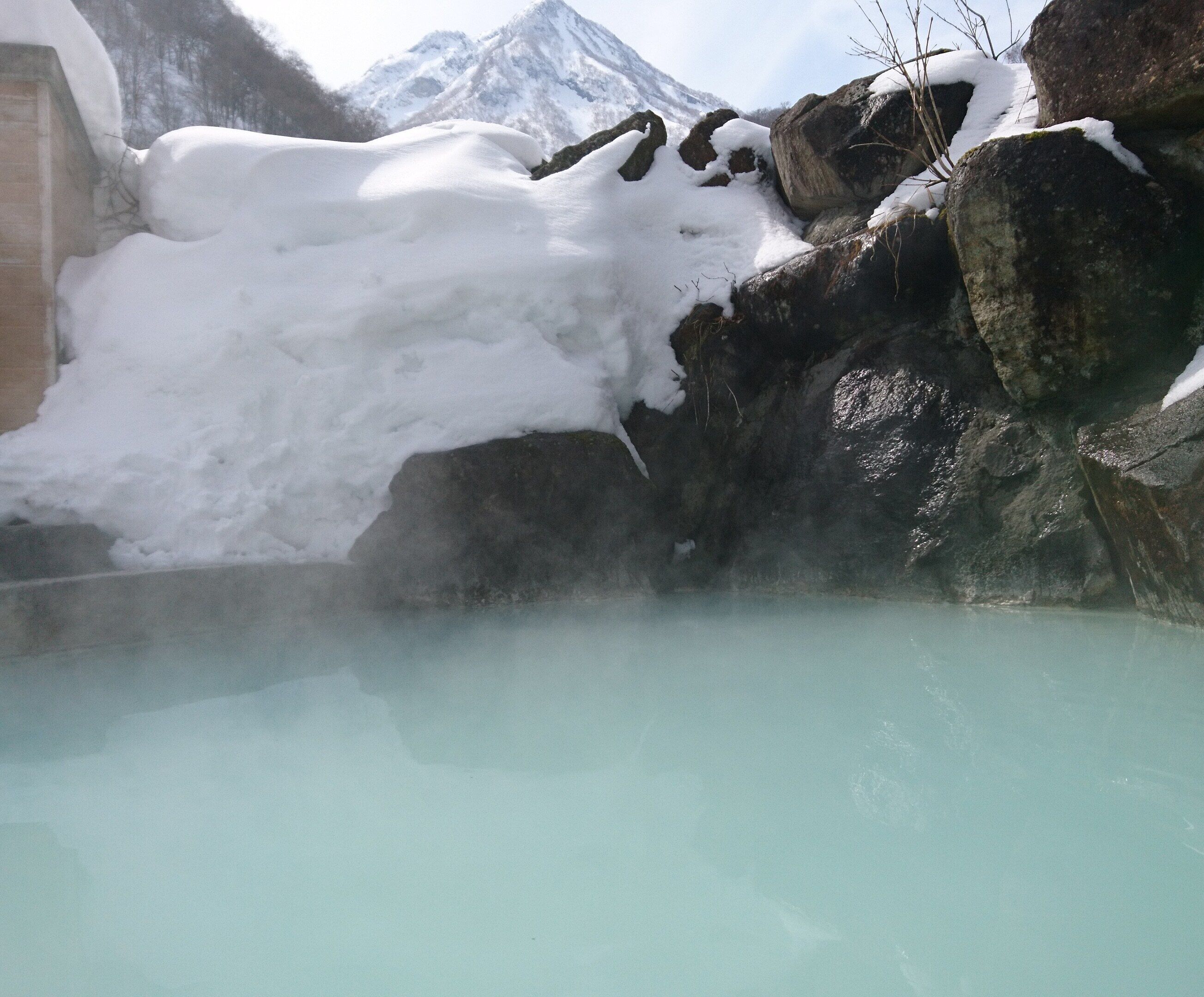 A hot spring with snow-covered rocks and a mountain in the background.