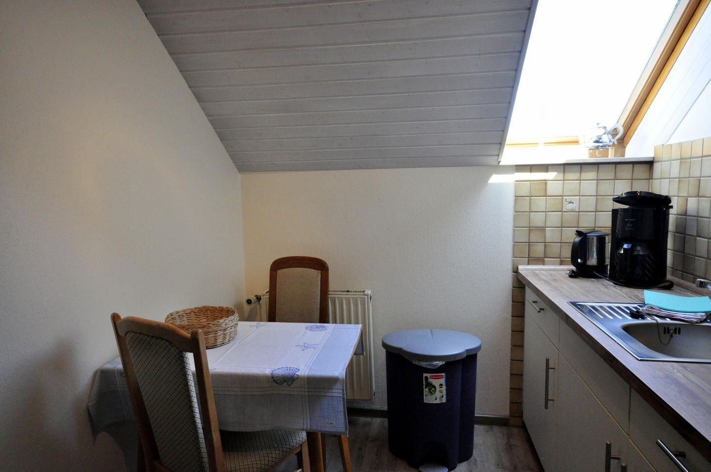 A compact kitchen with a table, chairs, a waste bin, and a coffee maker.