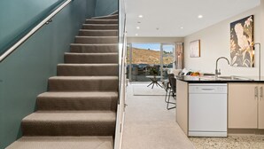A modern kitchen with a built-in dishwasher, a dining area with a table and chairs, and a staircase leading to an outdoor patio. - 2-BEDROOM REMARKABLES APARTMENT (Queenstown)