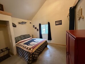 Un dormitorio con cama, cómoda, ventana con cortinas, un pez colgado en la pared y un marco de fotos.