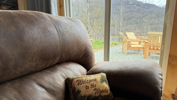 Een bruine leren bank met een kussen waarop staat 'Welcome to the Woods'.