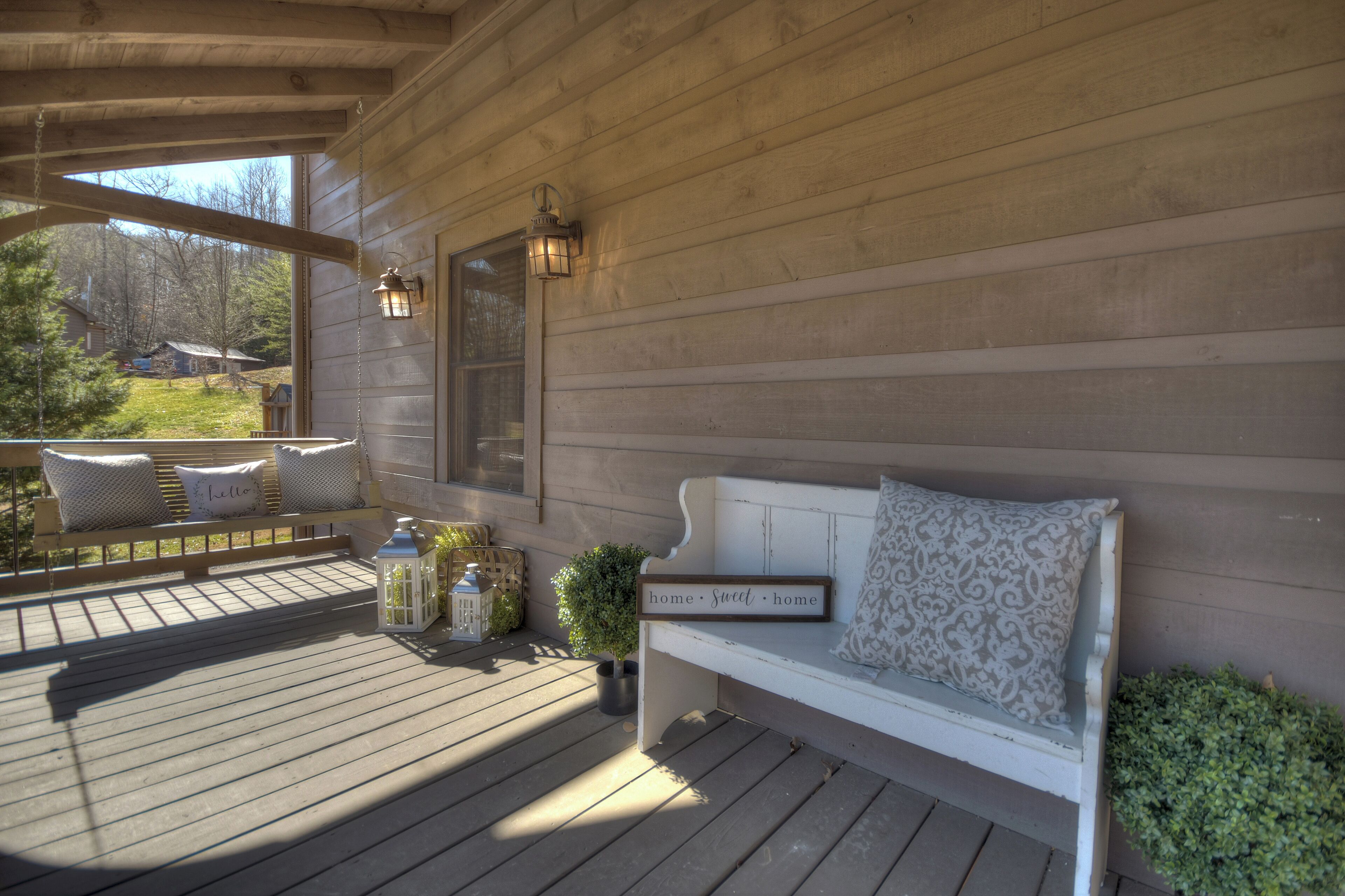 A wooden deck with a white bench, a small potted plant, and two lanterns.