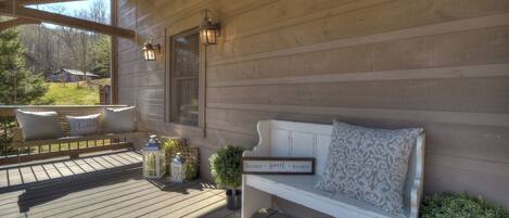 A wooden deck with a white bench, a small potted plant, and two lanterns.