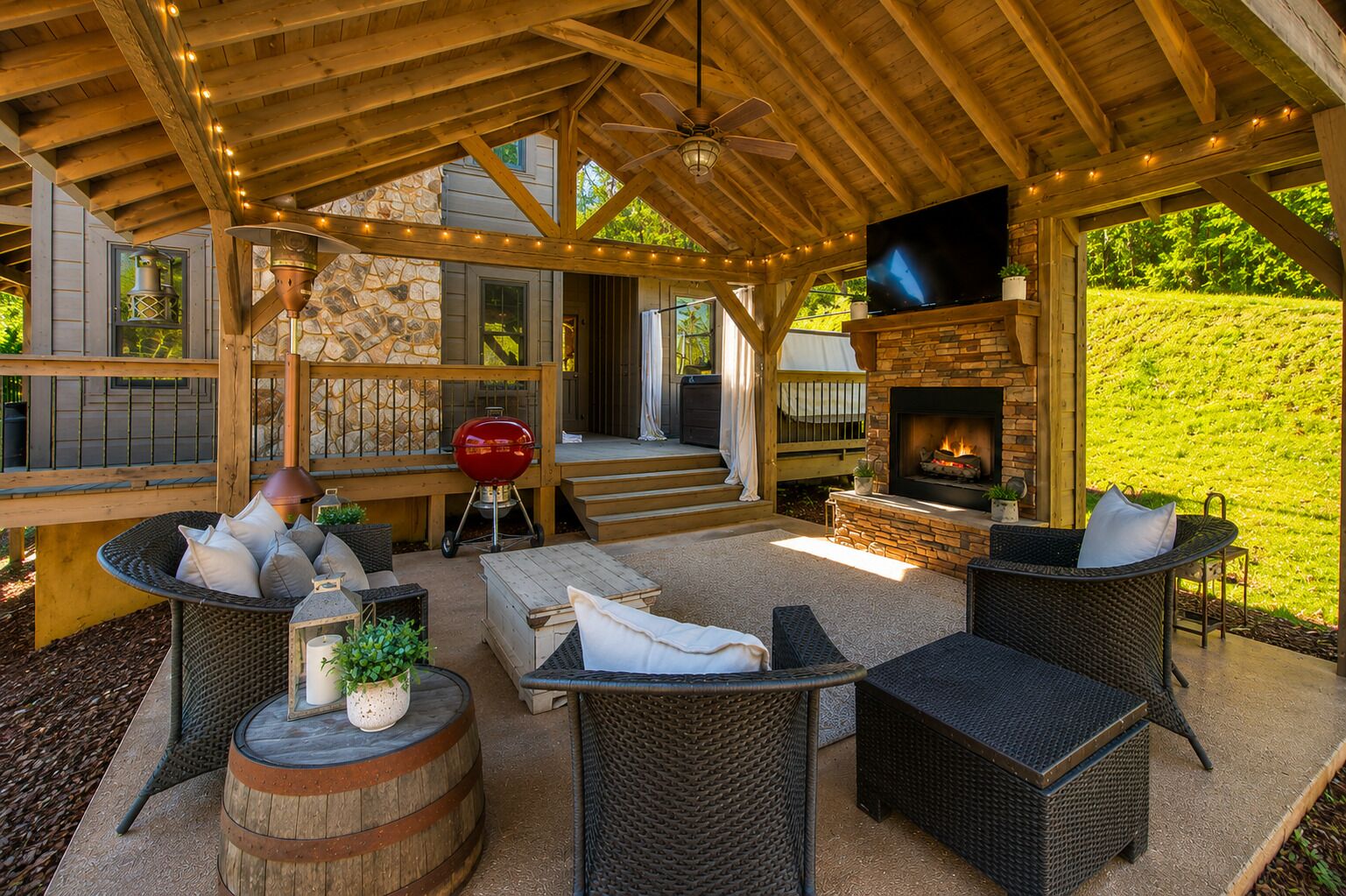 An outdoor patio with wicker furniture, a stone fireplace, and a TV mounted on the wall.