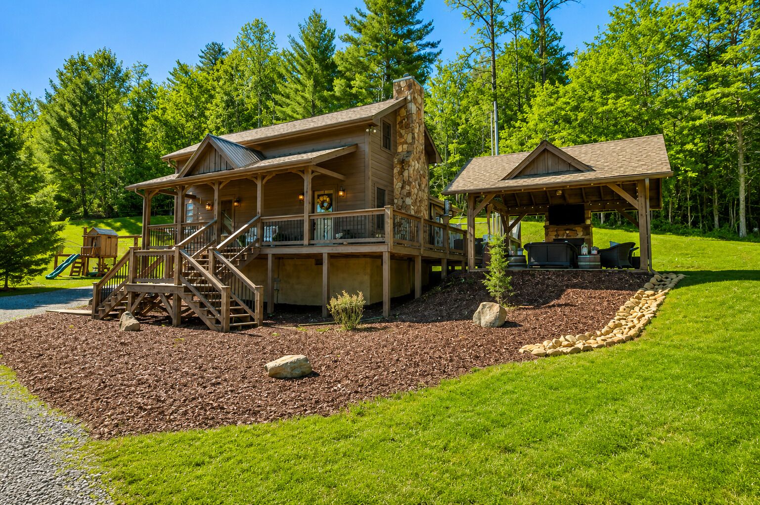 A two-story wooden cabin with a deck, a covered outdoor seating area, and a playground.