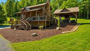 Une cabane en bois à deux étages, dotée d’une terrasse, d’un espace extérieur couvert avec des sièges et d’une aire de jeux.