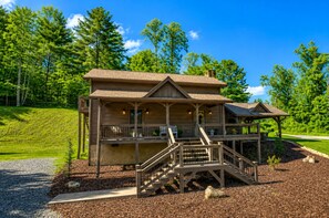 A two-story wooden lodge with a covered porch, a staircase, and a small gazebo.