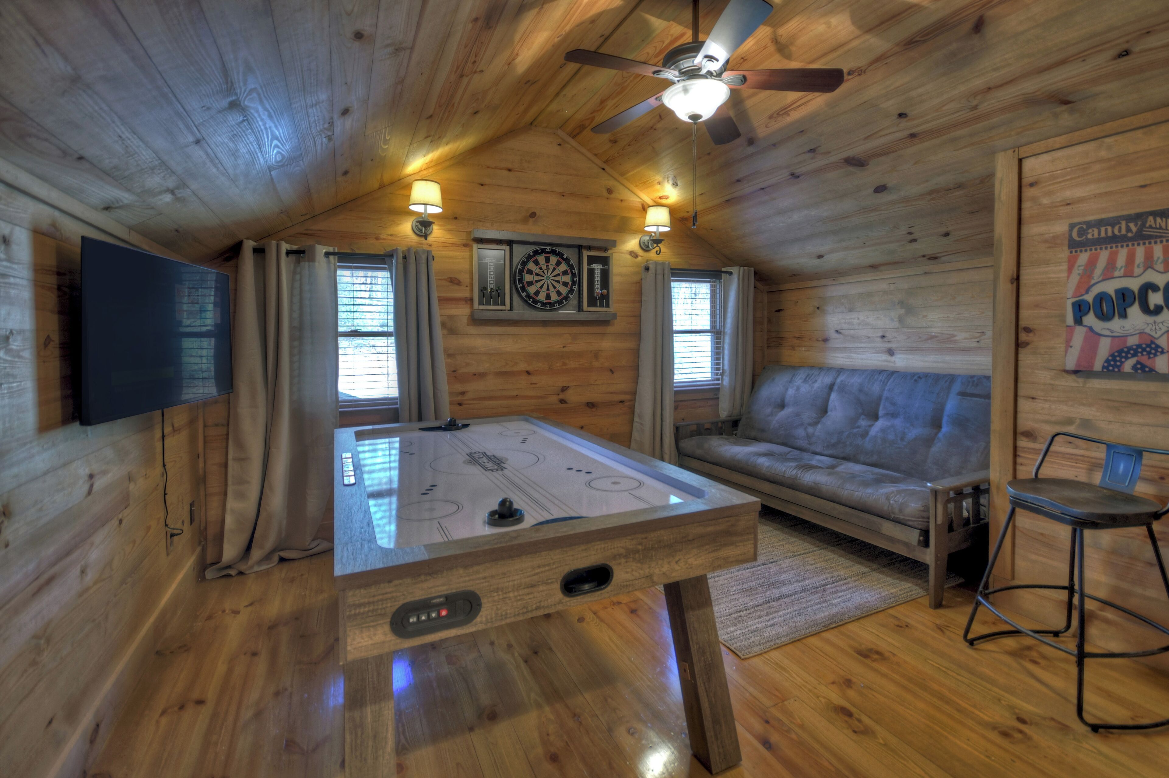 A cozy room with a foosball table, a sofa, a TV, and a dartboard.